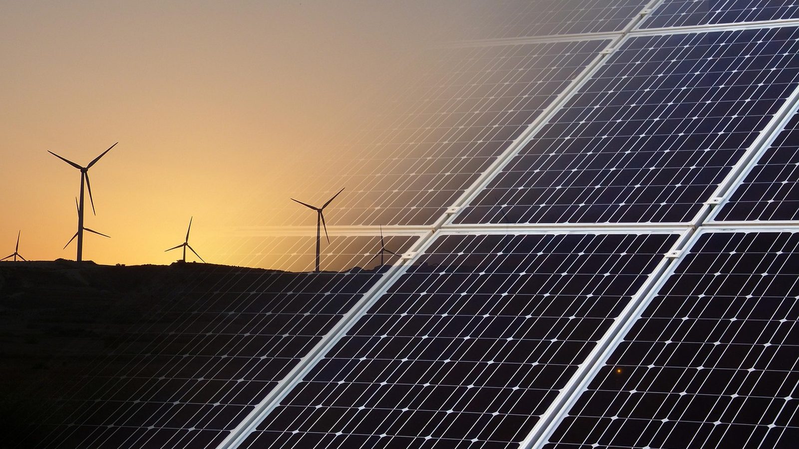 Solar panels in the foreground with wind turbines at sunset